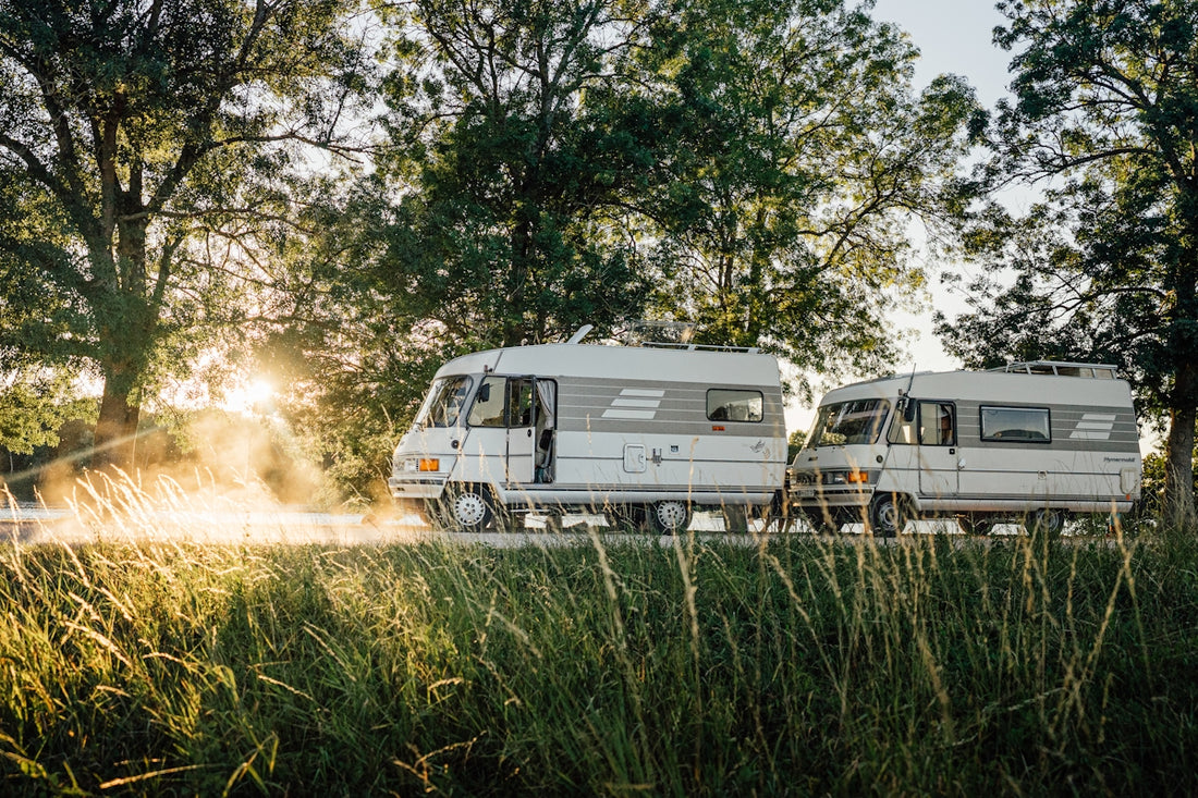 Two vintage vans travel down a sunny country road.