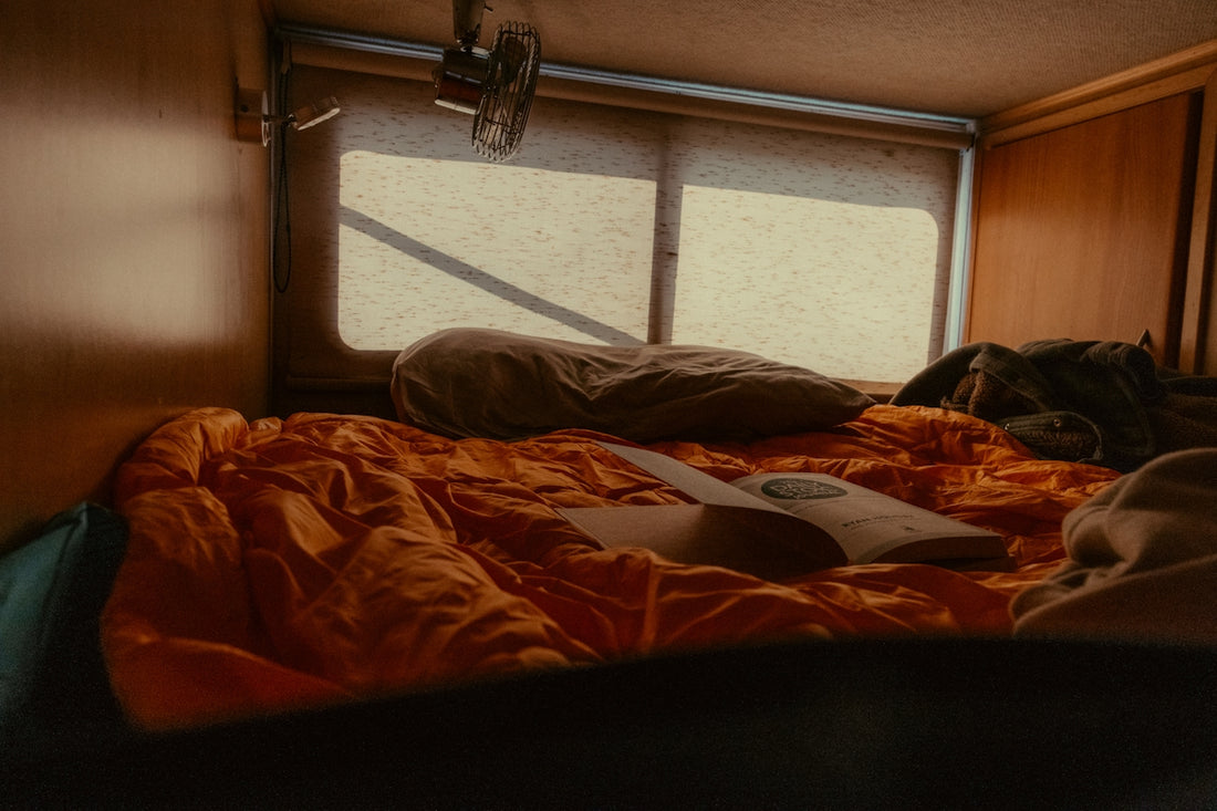 Camper bed with orange sleeping bag and window.